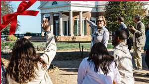Tour group sits by the fish pond at Monticello with the West Lawn and main house in the background