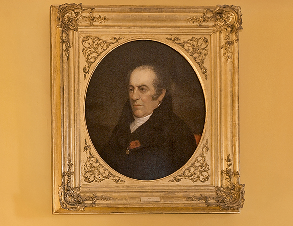 Painting of white man with dark eyes, balding at the front with thick brown sideburns in a dark, high-collared coat with a white neckerchief and a small red ribbon on its lapel