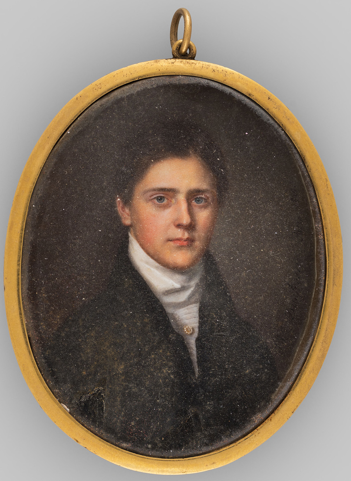 Miniature oval portrait of young white man with dark blue eyes and thick brown hair in a dark coat with a white neckerchief and a small circular pin with pearls