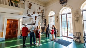 Two children, their parents, and a grandmother listen to a tour guide describe objects in the Entrance Hall of Monticello