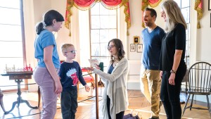 Adults and children listen to a tour guide who is showing objects to the children in Monticello's Parlor