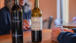 Wooden table with two bottles of Jefferson Vineyards wine and two people enjyoing award-winning wine