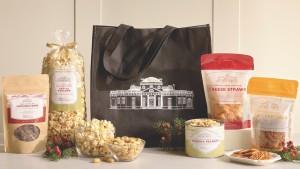 A vignette showing the charcoal-colored tote with a large image of Monticello flanked by four type of Monticello snacks (chocolate bark, popcorn, cheese straws, and spicy pretzels)