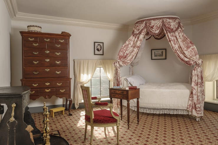 A bedroom curtained bed, a carpet, a tall chest of drawers, and a low window typical of Monticello's second floor
