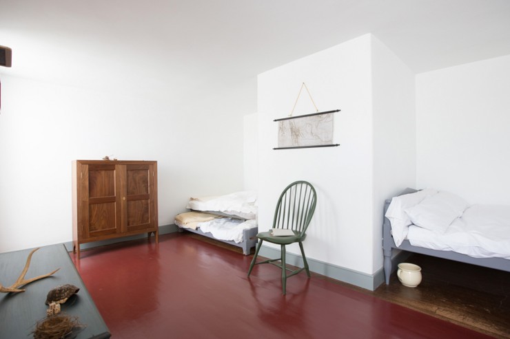 A bedroom with two alcove beds, a cabinet chest, a green chair, and part of a table showing an antler, a turtle shell, a nest, and a set of dice