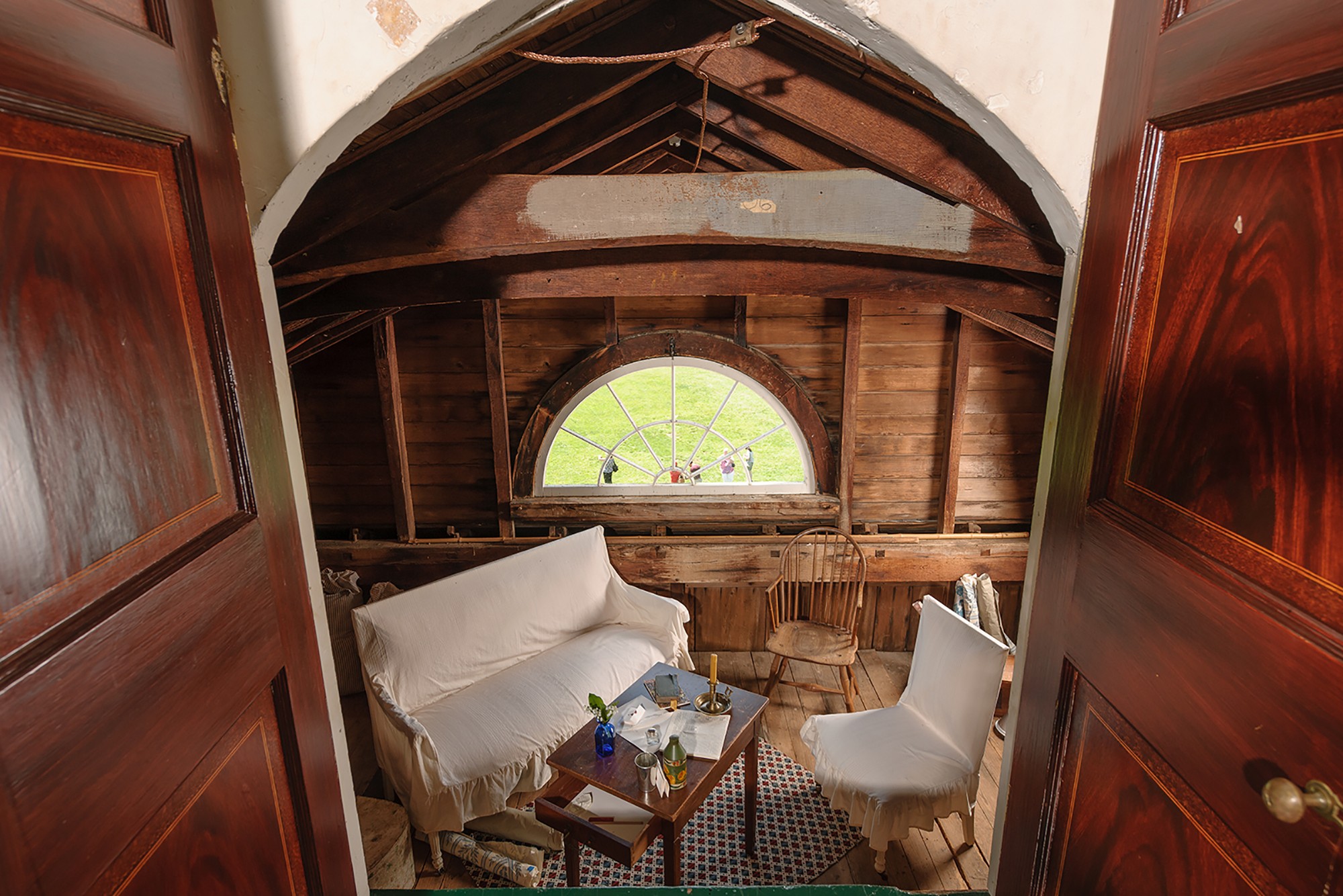 A door leads down to an attic space with a semicircular window and a set of old furniture