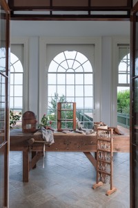 View through open doors to a large wooden bench with work tools within a glass-encased space